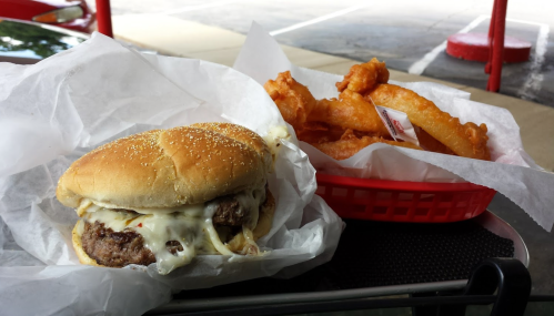 A cheeseburger with melted cheese on a sesame seed bun next to a basket of crispy onion rings.