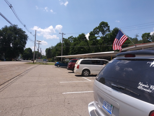 A parking lot with several vehicles, including a minivan with an American flag, under a clear blue sky.