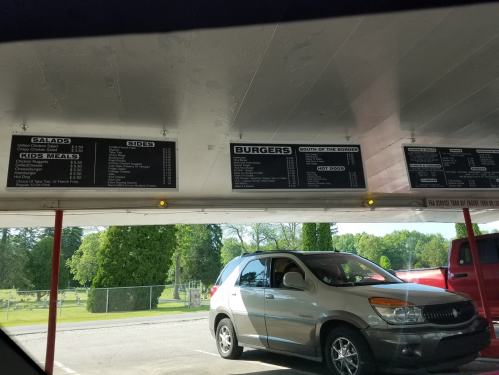 Menu board displaying food options like salads, sides, kids meals, and burgers at a drive-in restaurant. A car is parked below.