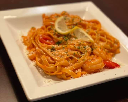 A plate of creamy fettuccine pasta garnished with lemon slices, red peppers, and parsley.