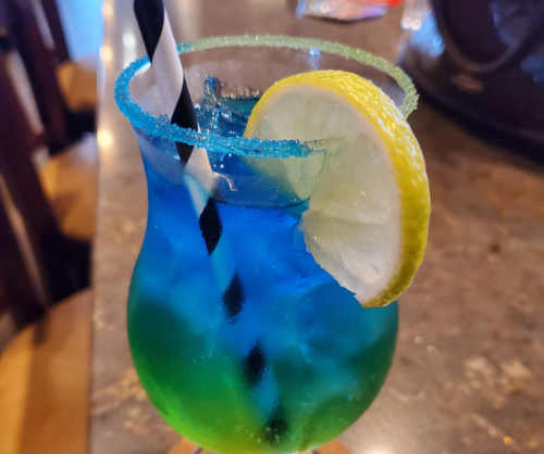 A colorful cocktail in a glass with a blue and green gradient, garnished with a lemon slice and a striped straw.