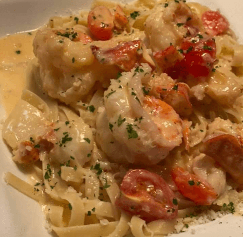 Creamy fettuccine pasta topped with shrimp, cherry tomatoes, and parsley in a white sauce.