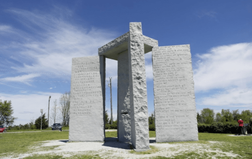 A large stone monument with inscriptions on multiple sides, set against a blue sky and green landscape.