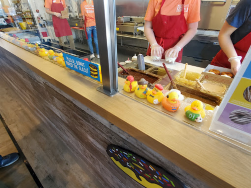 A counter with staff preparing food, featuring colorful rubber ducks lined up in front.