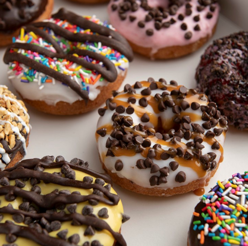 A variety of colorful donuts topped with sprinkles, chocolate chips, and drizzles, arranged in a box.