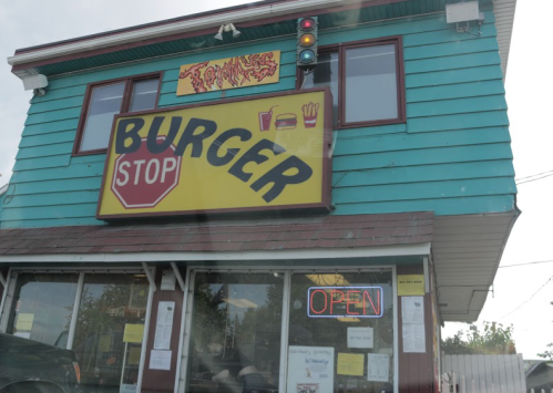 A colorful burger restaurant with a large "Burger Stop" sign and an open neon sign in the window.