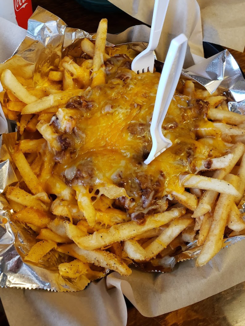 A large serving of loaded fries topped with melted cheese and ground beef, served with two plastic forks.