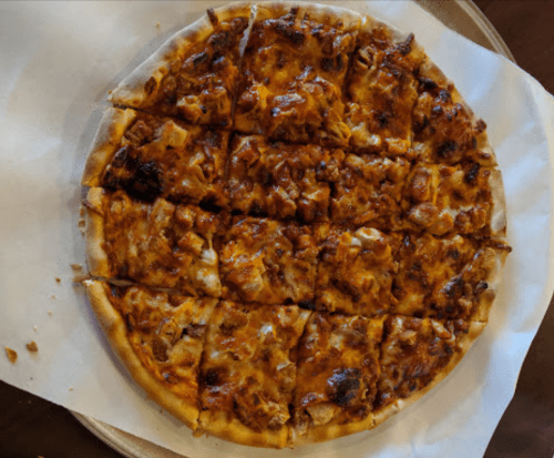 A round pizza with a golden crust, topped with melted cheese and chunks of meat, cut into square slices.