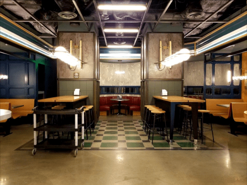 Modern restaurant interior featuring wooden tables, bar stools, and a cozy booth area with a checkered floor.