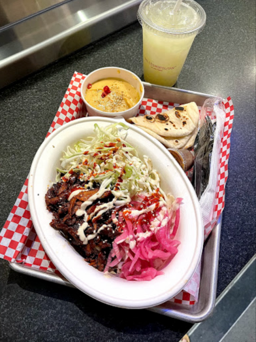 A tray with a bowl of meat, pickled onions, cabbage, a side of sauce, a flatbread, and a drink.