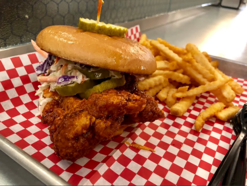 A crispy chicken sandwich with pickles and coleslaw, served with crinkle-cut fries on a red and white checkered tray.