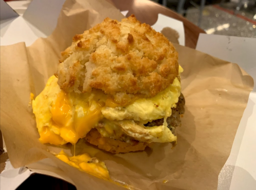 A hearty breakfast sandwich with a fluffy biscuit, scrambled eggs, and melted cheese, served on a paper wrapper.