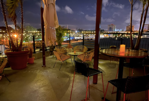 Cozy outdoor seating area at night, with string lights and city skyline in the background.