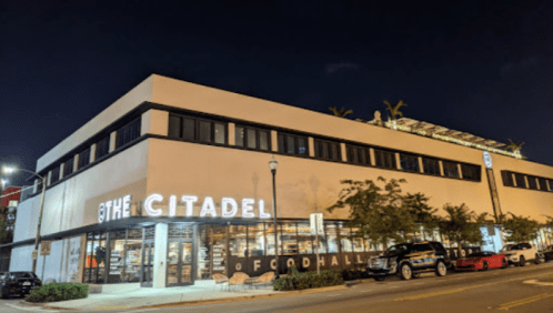 Exterior view of The Citadel building at night, featuring large windows and illuminated signage.
