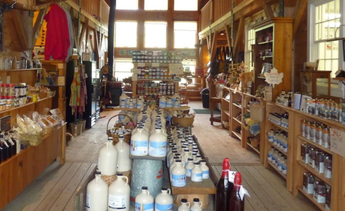 A rustic store interior with wooden shelves filled with various jars, bottles, and products in a bright, spacious setting.