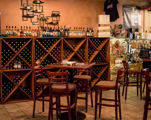 Cozy wine shop interior with wooden wine racks, bottles, and a small table with chairs. Warm, inviting atmosphere.