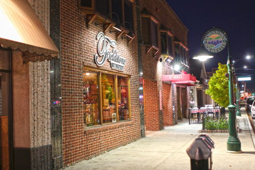 A brick storefront at night, featuring "Picklehome" signage, with outdoor seating and streetlights illuminating the scene.