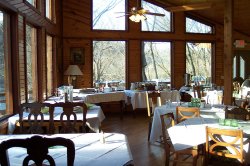 Cozy restaurant interior with wooden walls, large windows, and tables set for dining, featuring a buffet setup.