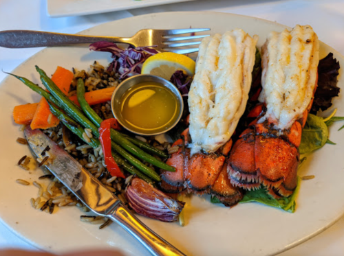 Grilled lobster tails served with rice, green beans, carrots, and a lemon wedge on a white plate.