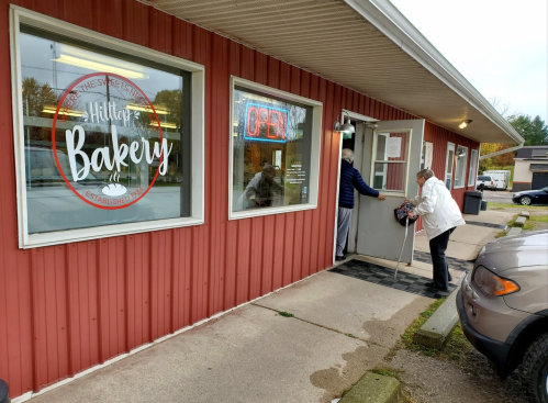 A woman enters Hilltop Bakery, which has an "Open" sign, while another woman stands at the door.