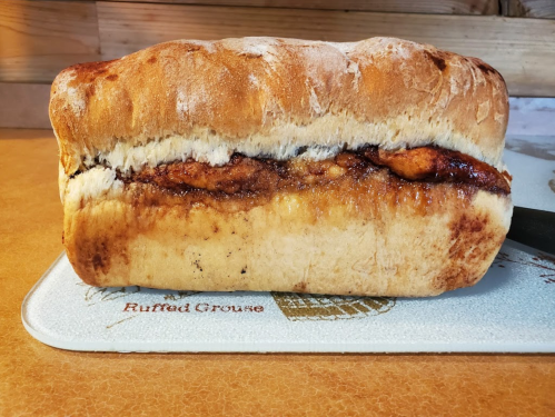 A loaf of bread with a visible layer of cinnamon filling peeking through the top crust, resting on a cutting board.