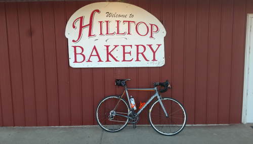 A bicycle parked in front of the Hilltop Bakery sign on a red wooden wall.