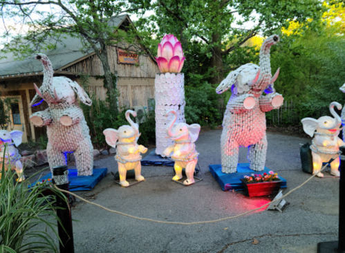 Colorful elephant sculptures made of various materials, illuminated with lights, set in a garden-like area.