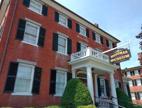 Historic red brick building with white trim, featuring large windows and a sign for the Woodman Museum.