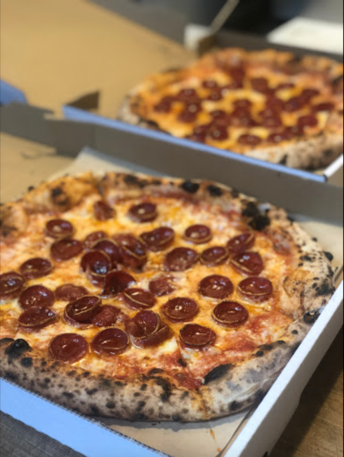 Two pizzas in cardboard boxes, one with a golden crust topped with pepperoni slices and melted cheese.