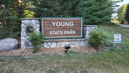 Sign for Young State Park, featuring a wooden board with stone accents, surrounded by greenery.