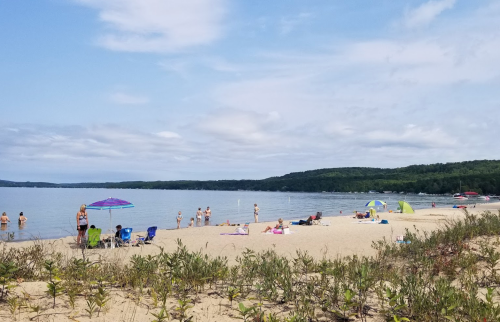 A sandy beach with people enjoying the water, umbrellas, and tents under a partly cloudy sky.