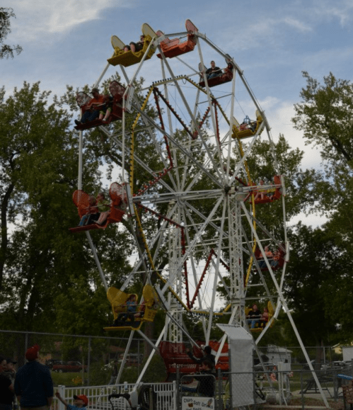 A colorful Ferris wheel with riders enjoying the view, set against a backdrop of trees and a cloudy sky.