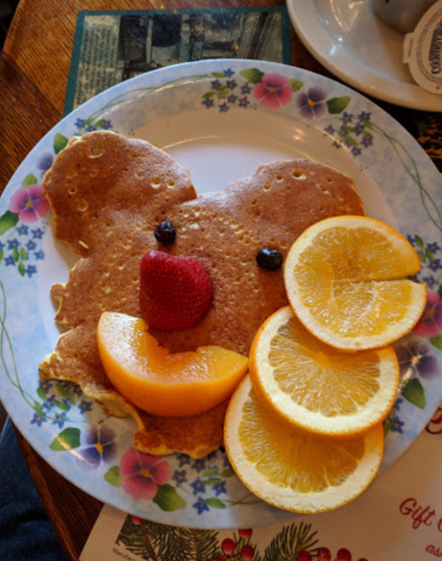 A plate of pancakes shaped like a bear's face, decorated with fruit slices for eyes and mouth.