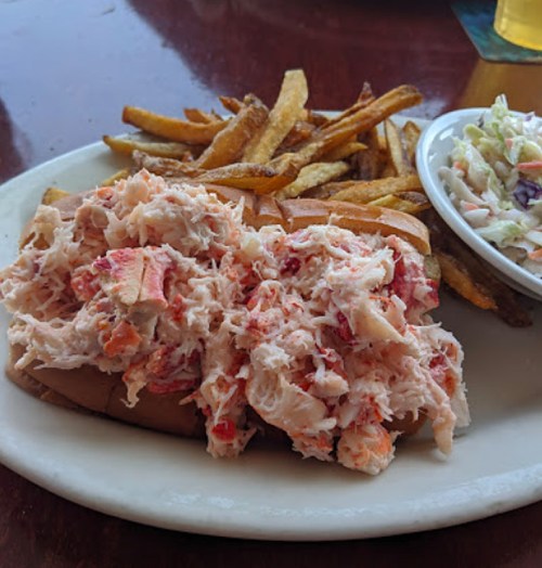 A lobster roll filled with lobster meat, served with fries and a side of coleslaw on a white plate.