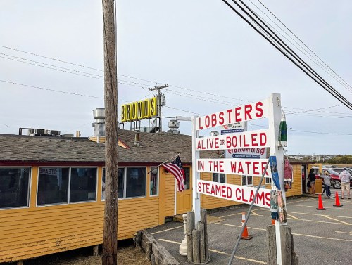 A seafood restaurant with a sign advertising live lobsters and steamed clams, featuring a yellow exterior and American flag.