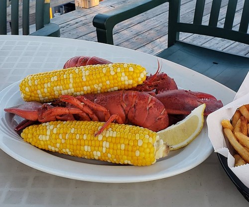 A plate with two lobsters, corn on the cob, and a lemon wedge, set on a table outdoors.