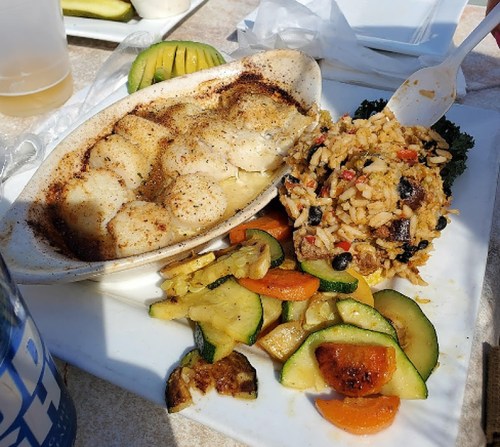 A plate featuring baked scallops, seasoned rice with black beans, and a variety of sautéed vegetables.