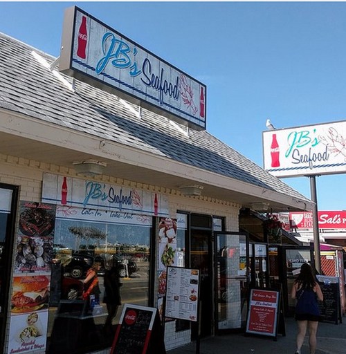Exterior of JB's Seafood restaurant with signage and a person walking by. Bright, sunny day.