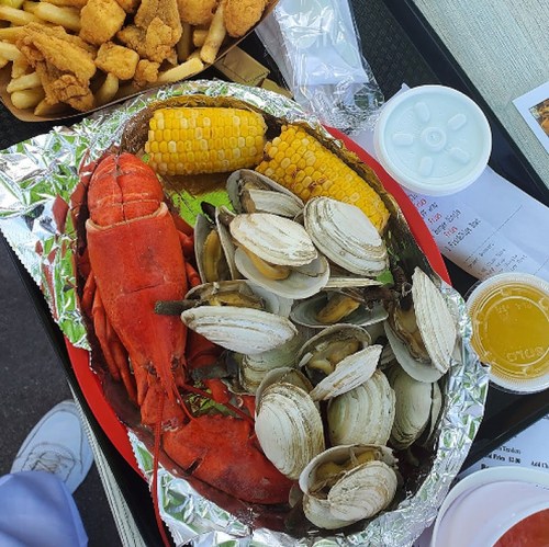 A seafood platter featuring lobster, clams, corn on the cob, fries, and a drink on a tray.
