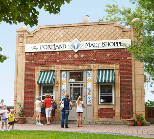 A charming brick building with a sign reading "The Portland Malt Shoppe," featuring people enjoying ice cream outside.