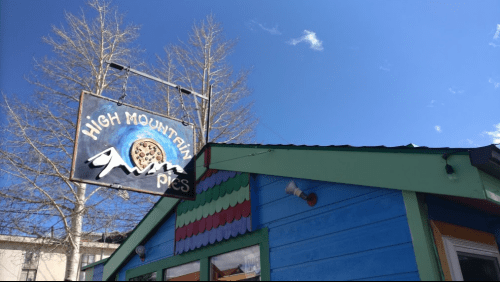 Sign for "High Mountain Pies" on a colorful building under a clear blue sky with a few clouds.
