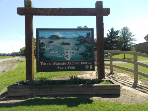 Sign for Toltec Mounds Archeological State Park, featuring a scenic illustration and surrounded by greenery.