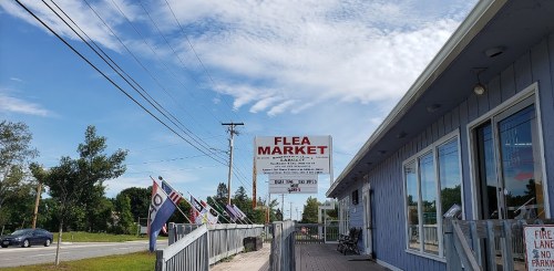 A blue building with a "Flea Market" sign, flags, and a clear sky in the background.