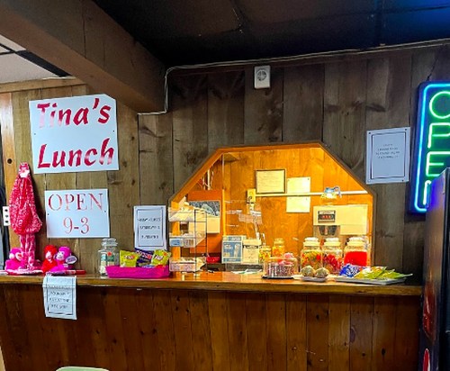 A cozy lunch counter with a wooden backdrop, featuring a neon "OPEN" sign and various snacks displayed.