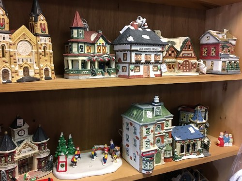 A display of colorful ceramic buildings and figurines on a wooden shelf, showcasing various architectural styles.