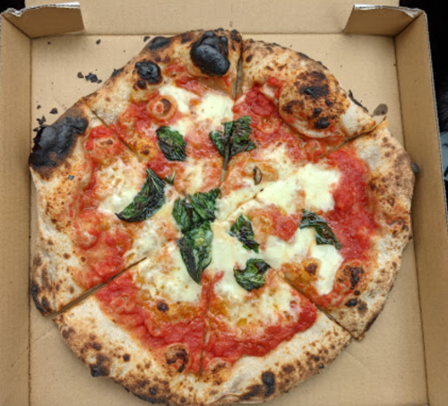 A freshly baked pizza with melted cheese, tomato sauce, and fresh basil, served in a cardboard box.