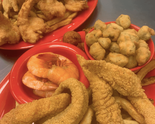 A vibrant spread of fried seafood, including shrimp, fish, and okra, served on red plates.
