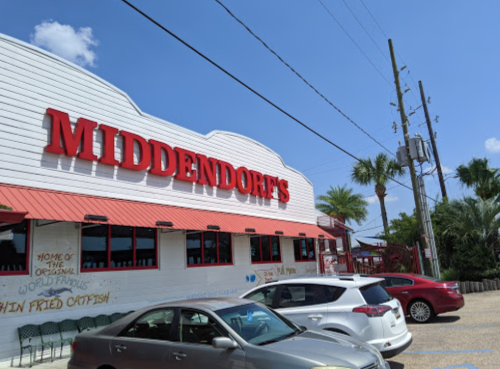 Exterior of Middendorf's restaurant with a red sign, palm trees, and parked cars under a blue sky.