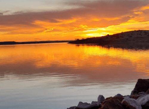 A serene sunset over a calm lake, with vibrant orange and yellow hues reflecting on the water's surface.