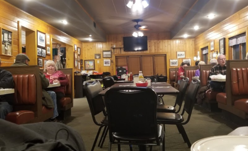 A cozy diner interior with wooden walls, booths, and patrons enjoying their meals. A TV is mounted on the wall.